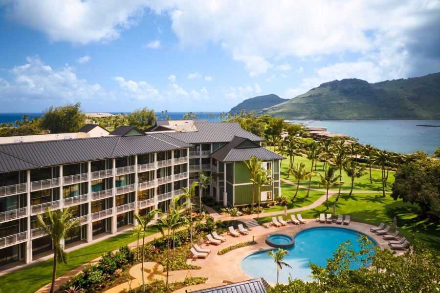 The pool and loungers at Hale Hōkūala Kauaʻi, with palm trees, ocean and mountains beyond.